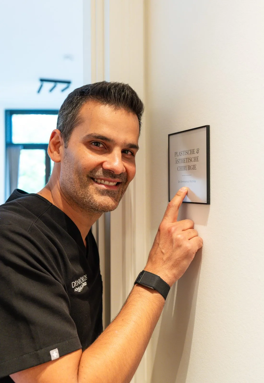 Dr. Emmanouil Nichlos am Praxisschild für Plastische & Ästhetische Chirurgie in Frankfurt